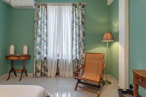 A hotel room with a bed, a chair, a table with candles, and a window with curtains.