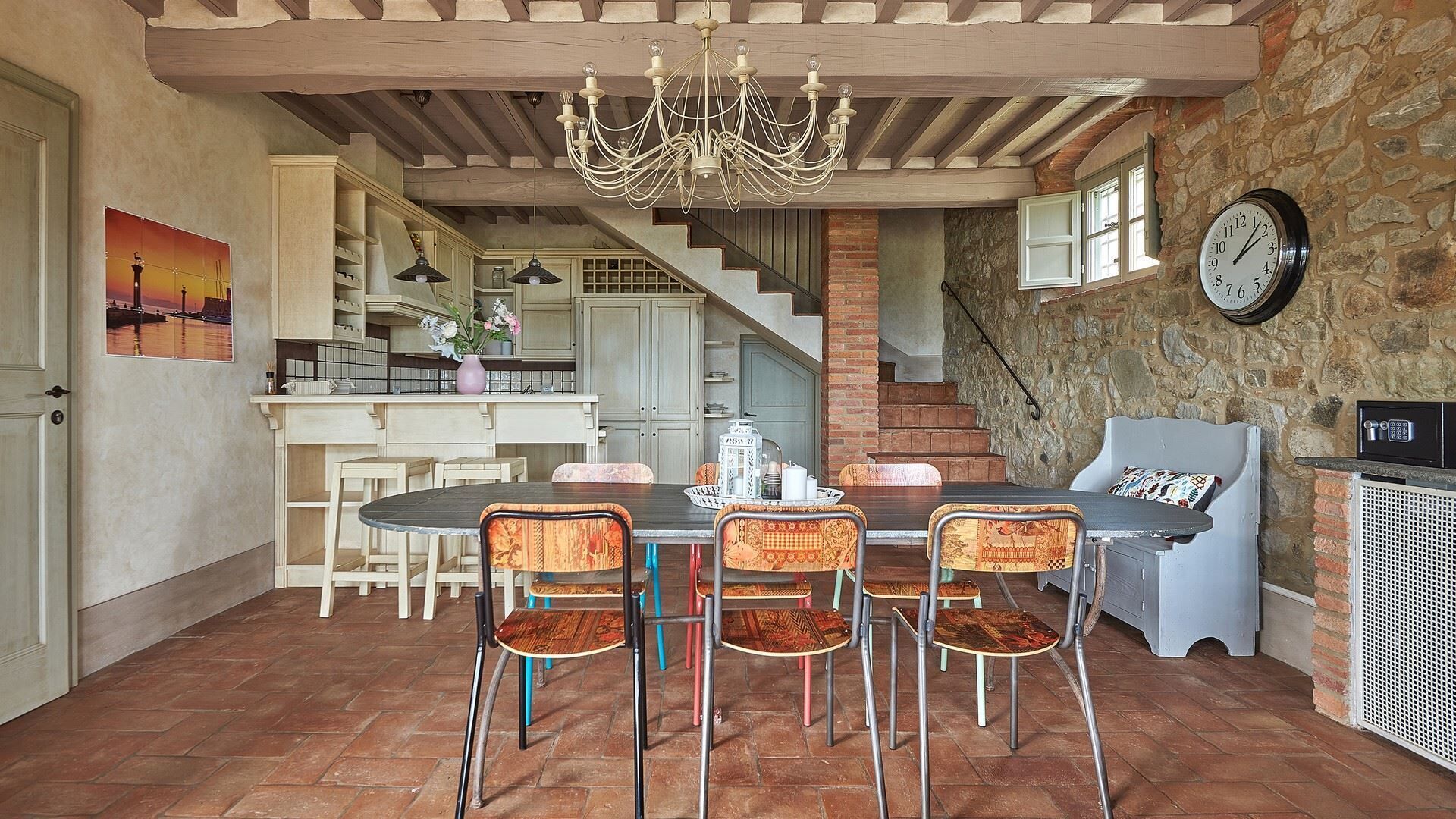 A spacious dining area with a large table and chairs, a chandelier, and a stone wall.