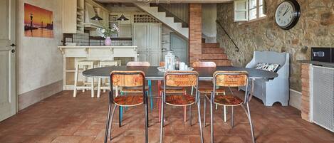 A spacious dining area with a large table and chairs, a chandelier, and a stone wall.