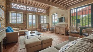 Ein geräumiges Wohnzimmer mit Steinwand, großen Fenstern und einem Fernseher.