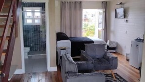A spacious living area with a wooden staircase, a bed, a grey sofa, and a patterned rug. - Pousada Toscana Cambará (Cambara do Sul)