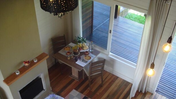 A dining area with a wooden table set for four, a fireplace, and a view of the outdoors through large windows. - Pousada Toscana Cambará (Cambara do Sul)