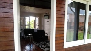 A wooden cabin with a dining area featuring a black and white checkered floor, a TV mounted on the wall, and a sliding glass door leading outside. - Pousada Toscana Cambará (Cambara do Sul)