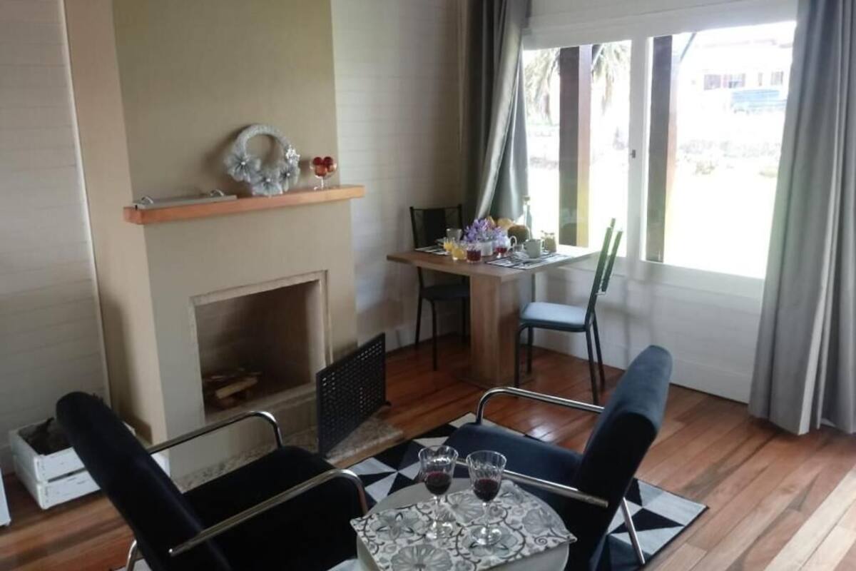 Um quarto com lareira, uma mesa de jantar com cadeiras e uma janela com cortinas.