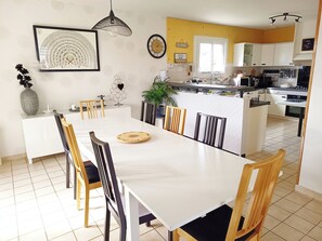 Una cocina moderna con armarios blancos, un comedor con mesa y sillas blancas, y una isla de cocina con un fregadero y estufa.