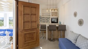A modern kitchen with a wooden door, bar stools, a blue sofa, and a view of the outdoors.
