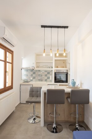 A modern kitchen with a central island, bar stools, and pendant lighting. - Theodora's Suite (Paros)