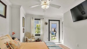 A bedroom with a bed, a ceiling fan, a TV, and a door leading to a balcony.