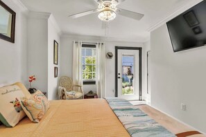 Una camera da letto con un letto, una ventola a soffitto, una TV e una porta che dà su un balcone.