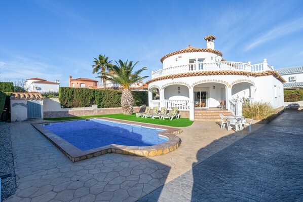 A villa with a swimming pool, a covered patio, and a well-maintained garden.