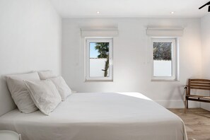 A bedroom with a bed, two windows, a chair, and a wooden floor.