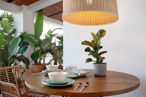 A round wooden table with a woven light fixture, a potted plant, and a notebook.