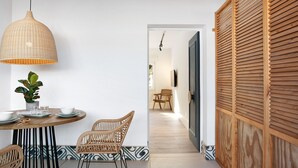 A dining area with a round table, wicker chairs, a hanging light fixture, and a potted plant.