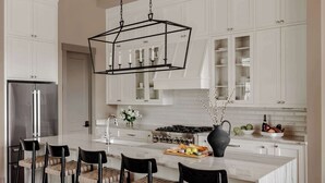 Una cocina moderna con armarios blancos, una isla central con taburetes de bar, un refrigerador de acero inoxidable y una estufa a gas.