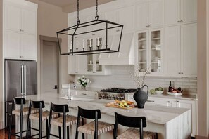 A modern kitchen with white cabinetry, a central island with bar stools, a stainless steel refrigerator, and a gas stove.