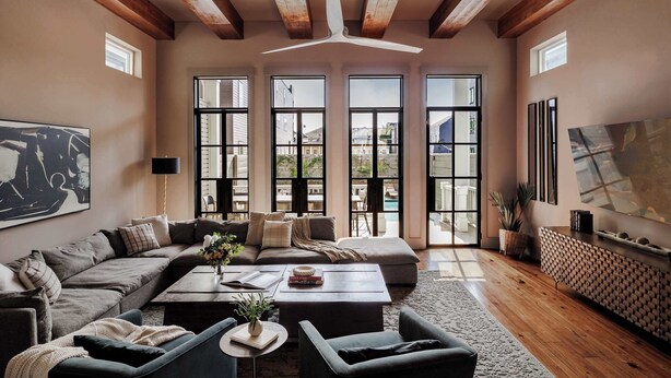 Un amplio espacio de sala con un sofá seccional grande, una mesa de centro y un televisor. Hay ventanas grandes y un ventilador de techo.