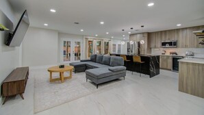 A modern living room with a grey sectional sofa, a wooden coffee table, and a TV mounted on the wall. - Central Convenience x Modern Luxury - Heart of Houston (Houston)