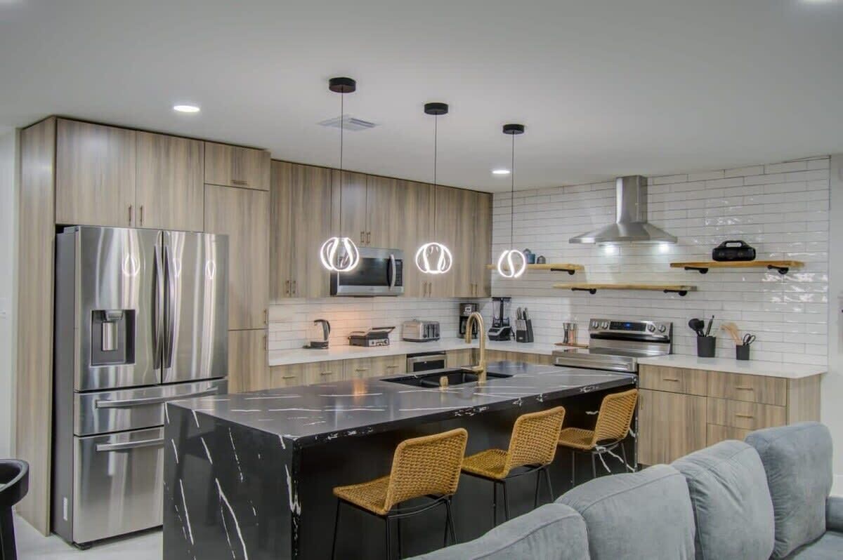 Una cocina moderna con una isla central, electrodomésticos de acero inoxidable y un sofá gris con sillas de mimbre.