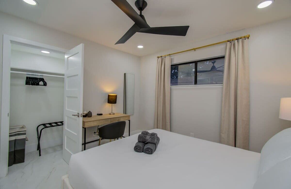 Ein Hotelzimmer mit Bett, Schreibtisch, Stuhl, Kleiderschrank, Deckenventilator und einem Fenster mit Vorhängen.