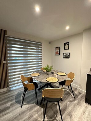 A dining area with a round table, six chairs, and a potted plant.