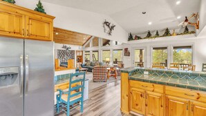 A spacious kitchen with wooden cabinets, a stainless steel refrigerator, and a large island with a green countertop. - Hot tub, ping pong, AC | 5 Suites (Sunriver)