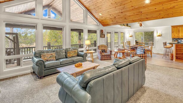 A spacious living area with large windows, a high wooden ceiling, and a cozy seating arrangement. - Hot tub, ping pong, AC | 5 Suites (Sunriver)