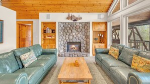 A cozy living room with a stone fireplace, leather sofas, and wooden ceiling beams. - Hot tub, ping pong, AC | 5 Suites (Sunriver)