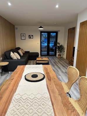 A modern living room with a wooden dining table, a sofa, and wicker chairs. - 2 Ashbrook Margaret - luxury 2 bed ground floor (Oxfordshire)