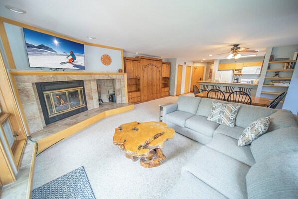 A living room with a fireplace, a large flat-screen TV, a wooden coffee table, and a sofa with patterned cushions. - Keystone Winter Stay | Balcony & Mountain Views (Keystone)