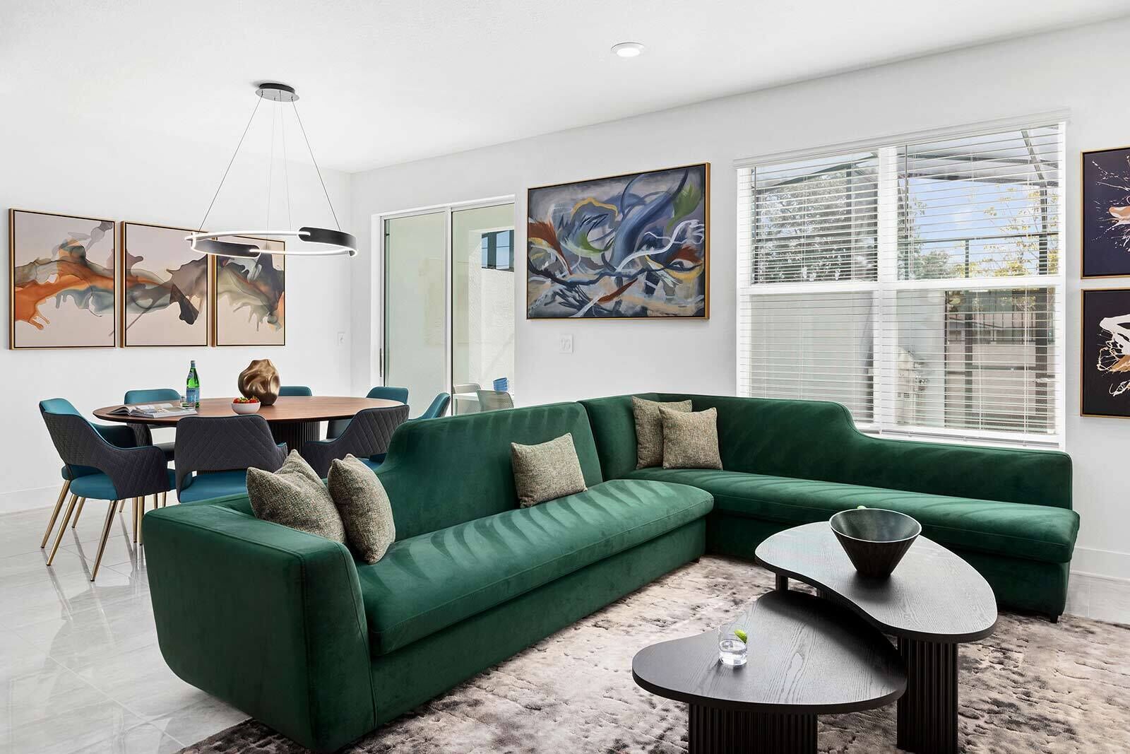 A modern living room with a green sectional sofa, a round coffee table, and a dining area with a table and chairs.