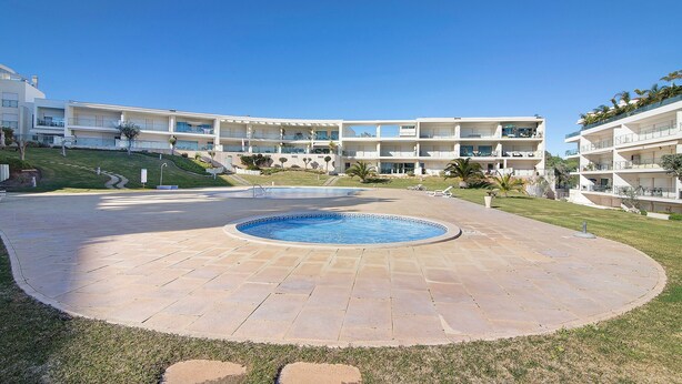 A pool area with a circular pool, a flat roof, and a building with multiple balconies.
