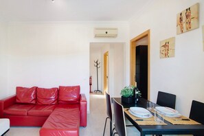 Un canapé en cuir rouge, une table à manger avec des assiettes et des verres, et un couloir menant à une autre pièce.