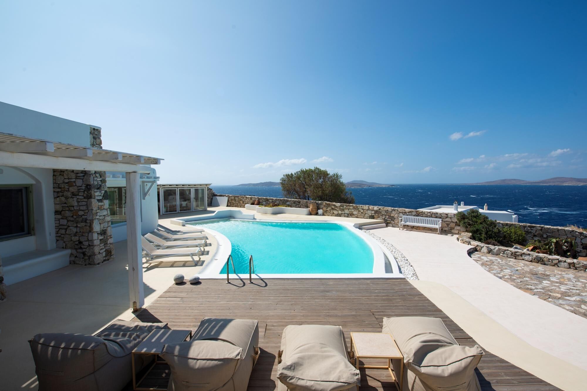A pool with a view of the sea, lounge chairs, and a stone wall.