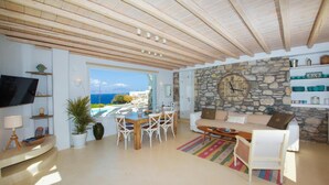 A spacious living area with a stone wall, a wooden ceiling, and a view of the sea. - Villa Magdalena Mykonos (Mykonos)