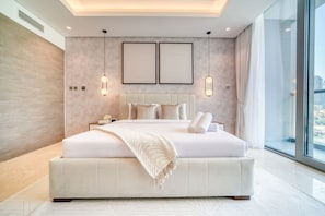 Quarto moderno com uma cama grande, duas luminárias fixadas na parede e vista para a cidade através de grandes janelas.