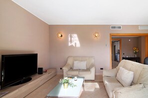 A living room with a flat-screen TV, two sofas, a coffee table with a plant, and wall-mounted lighting.