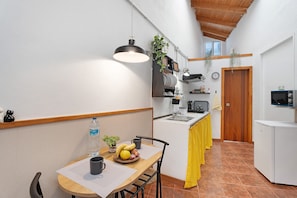 A compact kitchen with a dining table, chairs, a hanging light fixture, a sink, and a refrigerator.