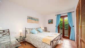 Un dormitorio con cama, mesitas de noche, escritorio, ventana con cortinas y puerta.