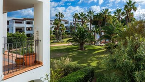 Un balcón con plantas en macetas, un césped cuidado y vistas a una zona residencial con palmeras y edificios.