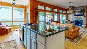 Una cocina amplia con una isla grande, armarios de madera y una chimenea de piedra. Hay un ventanal con vistas al exterior.