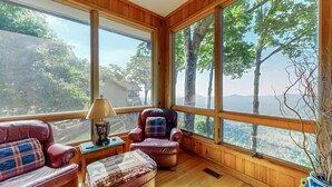 Una habitación acogedora con ventanas amplias, un sofá de cuero, un sillón escocés y suelo de madera.