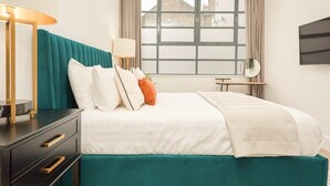 Hotellihuone, jossa on sänky, työpöytä, lamppu ja televisio.