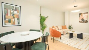 A modern living room with a round dining table, green chairs, a sofa, and a coffee table. - Modern Marylebone apartment with balcony (London)