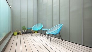 A balcony with a wooden floor, two blue chairs, a small table, and potted plants. - Modern Marylebone apartment with balcony (London)