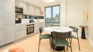 A modern kitchen with grey cabinets, a microwave, and a dining area with a round table and green chairs. - Modern Marylebone apartment with balcony (London)