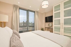 Een hotelkamer met een groot bed, een aan de muur bevestigde televisie en uitzicht op de stad door het raam.