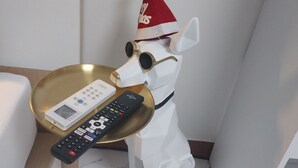 En hvid hundefigur med julehat sidder på et hvidt gulv og holder en fjernbetjening.