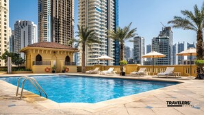 A swimming pool with lounge chairs and umbrellas, surrounded by high-rise buildings. - Travelers Dubai Marina Hostel (Dubai)