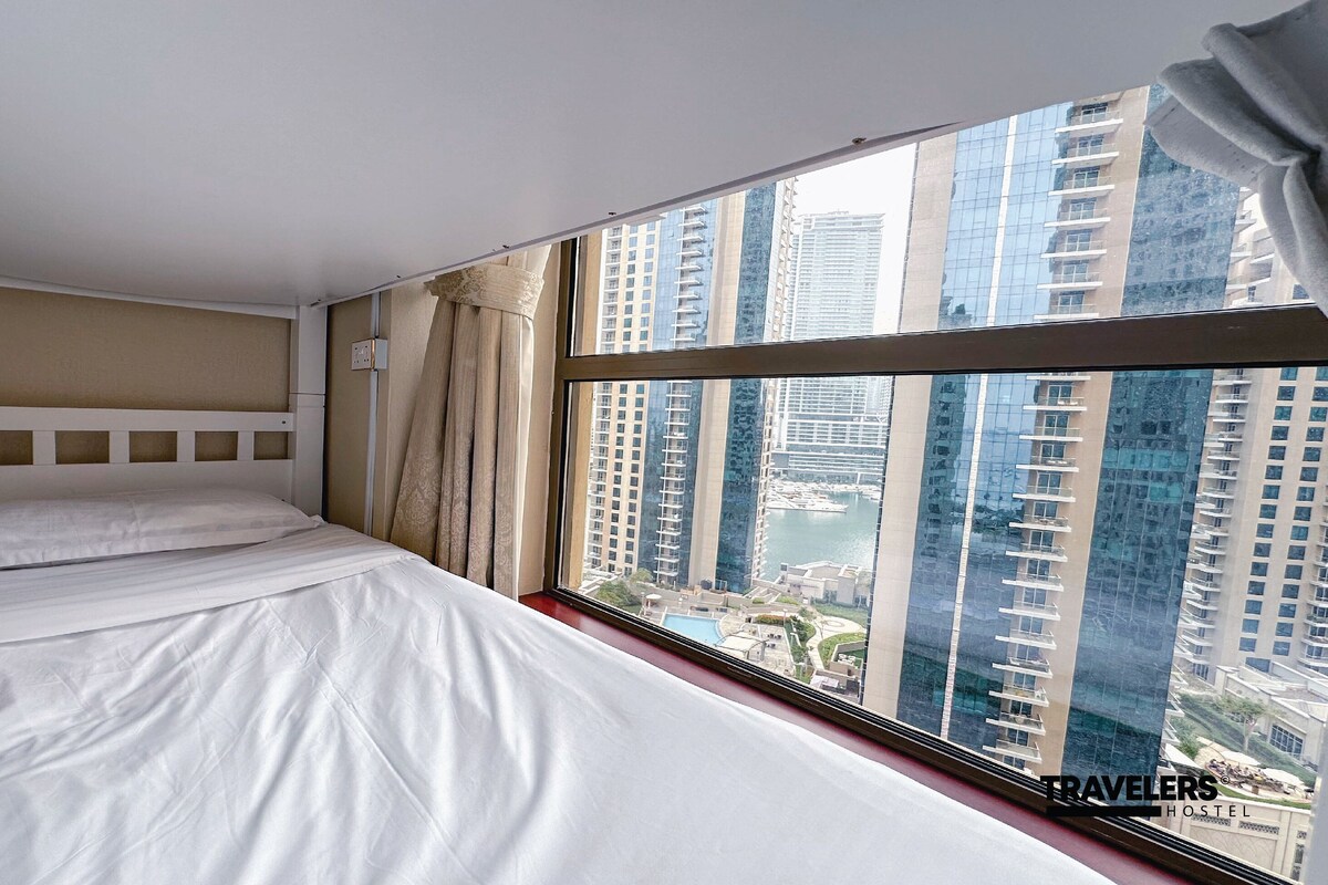 Habitación de hotel con una cama grande, vistas a rascacielos y una ventana con cortinas.