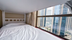 A hotel room with a large bed, a view of high-rise buildings, and a window with curtains. - Travelers Dubai Marina Hostel (Dubai)